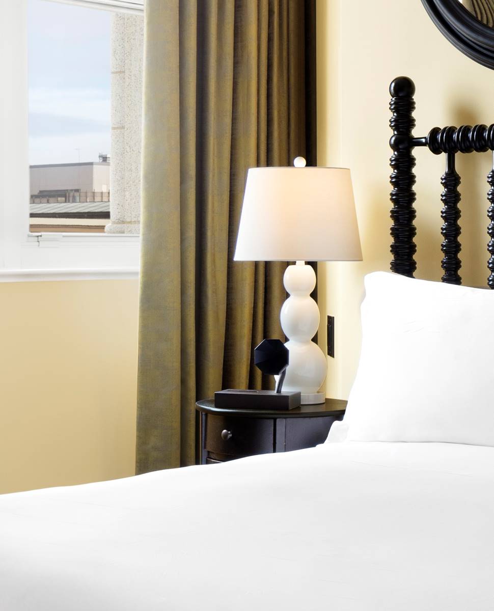 The bedroom of the First Lady Louisa Adams suite at Riggs DC, featuring luxurious bedding and elegant furnishings.