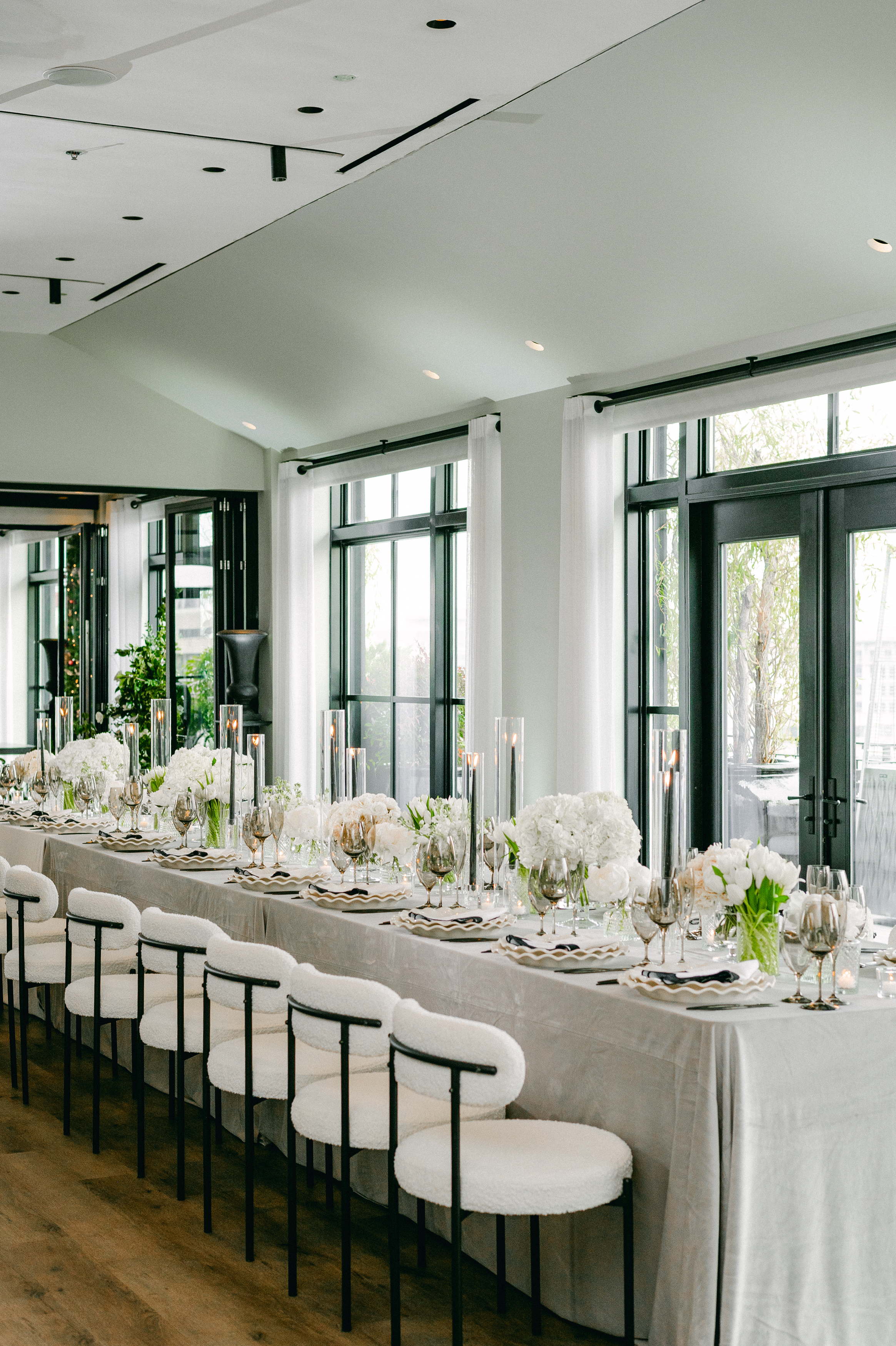 a long dining table set with white chairs, flowers, and candles