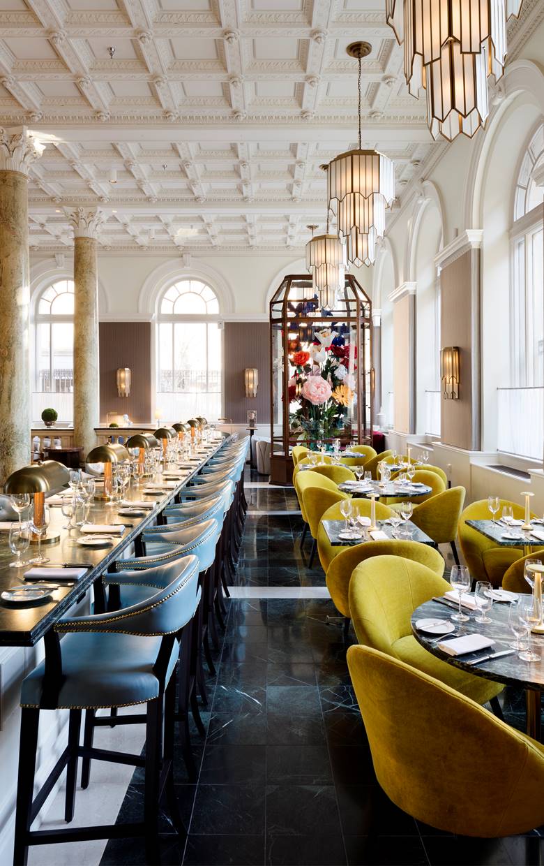 A large, opulent dining area at Riggs DC with grand columns and plush seating, featuring a large bouquet of flowers.