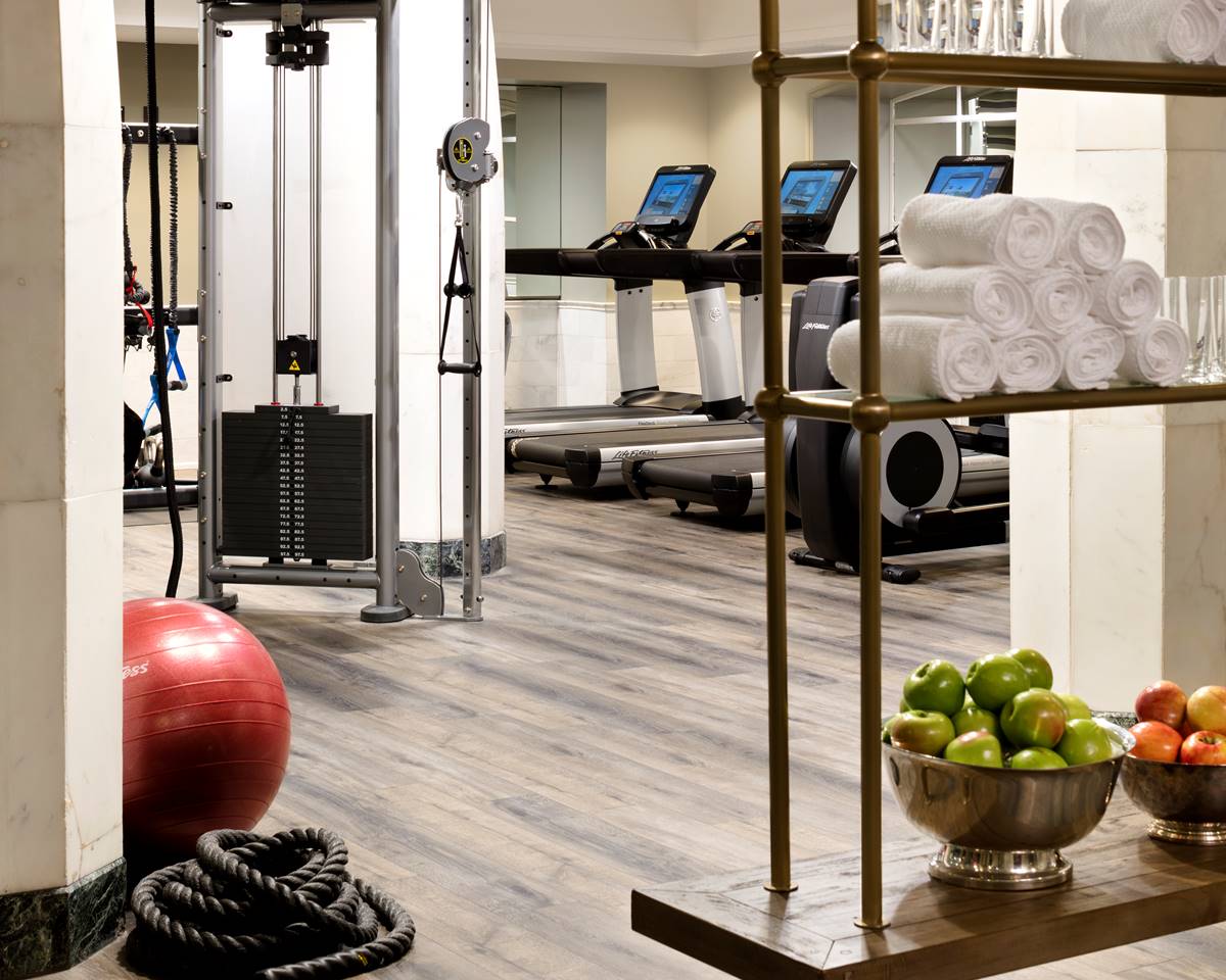 A modern gym at Riggs DC, equipped with state-of-the-art fitness machines, fresh fruit bowls and large mirrors.