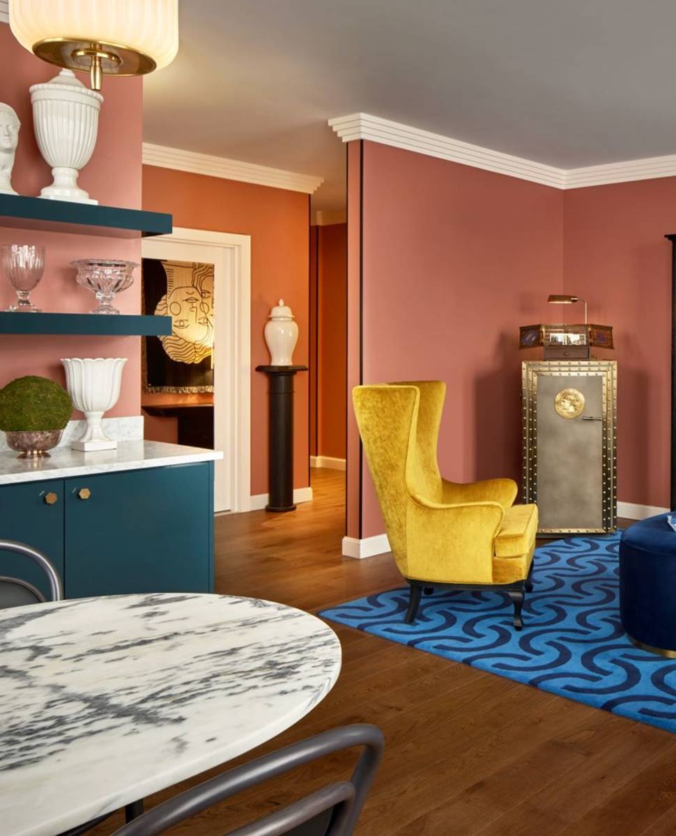 Boldly styled suite with yellow armchair, blue rug, marble table, and a vault-inspired minibar.
