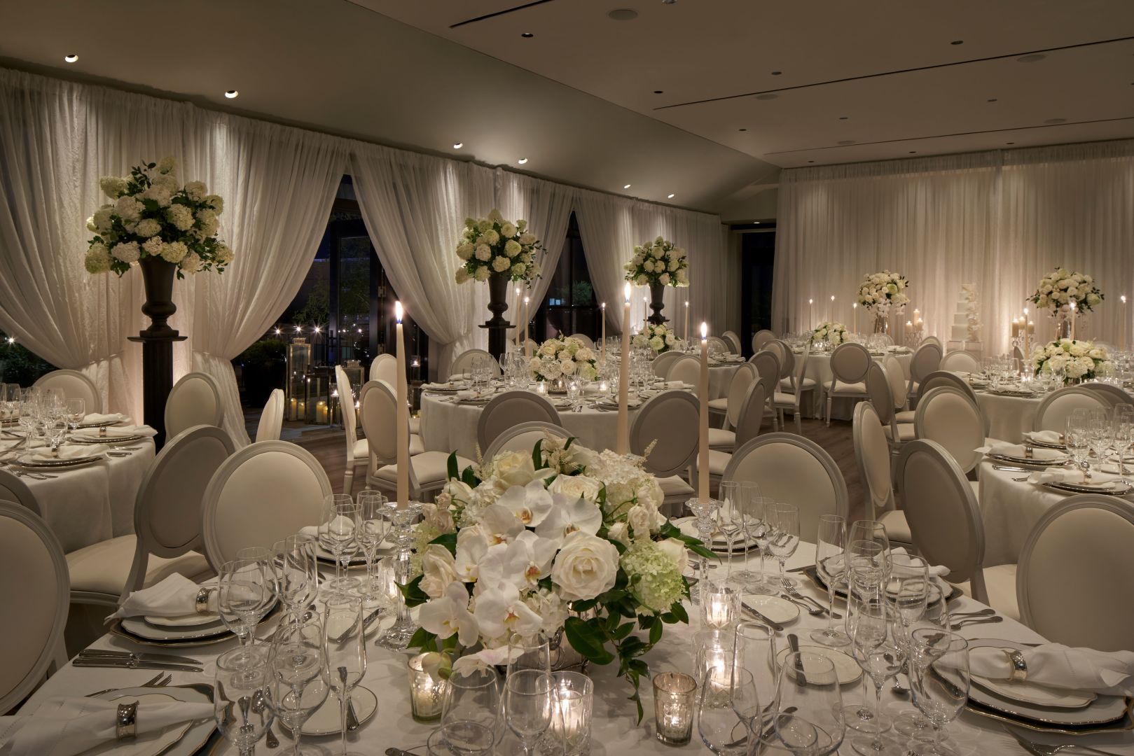 a formal dining room with white flowers, candles, and drapes