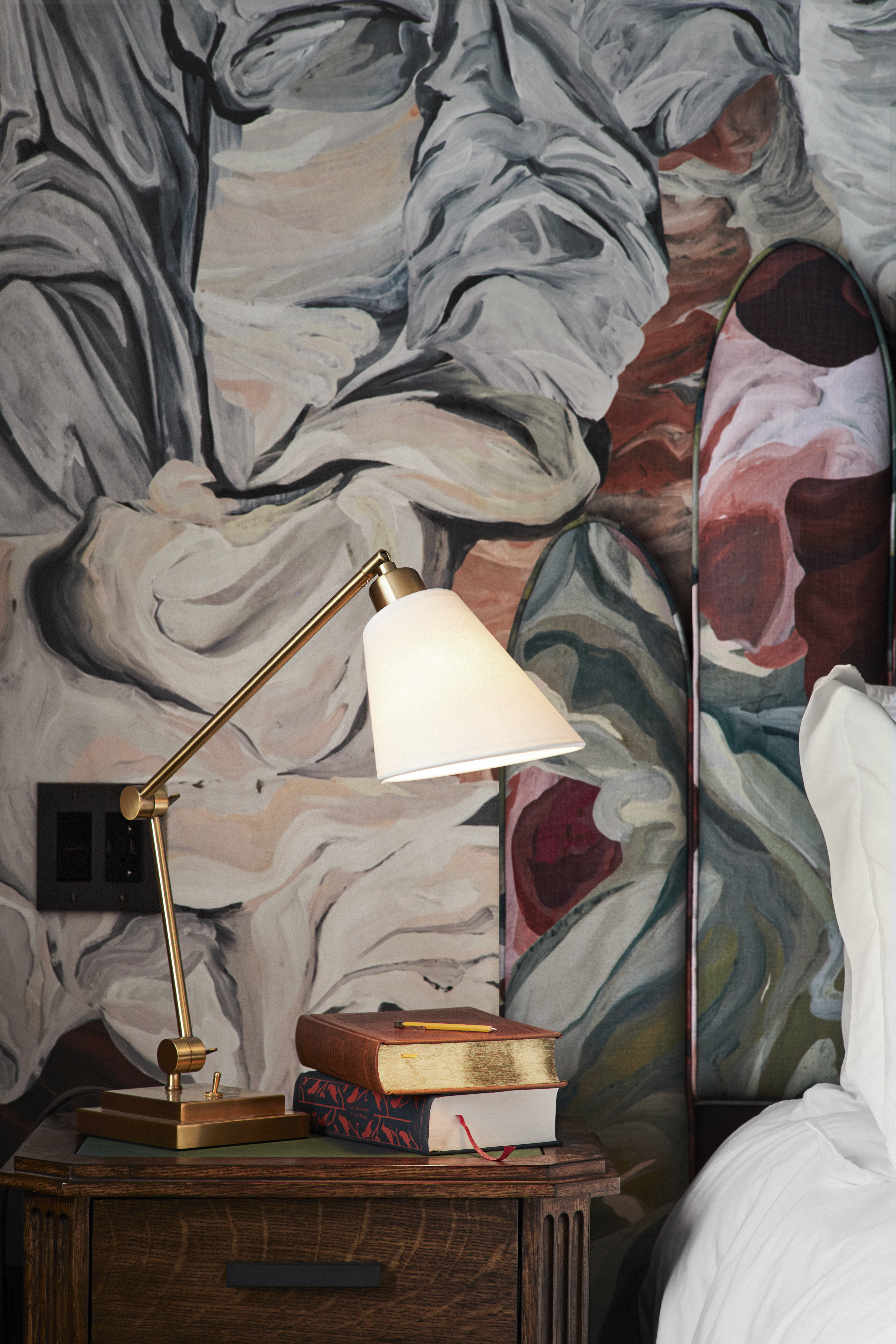 A close-up of a guest room nightstand, showcasing elegant decor elements including a gold lampshade and floral wallpaper. 