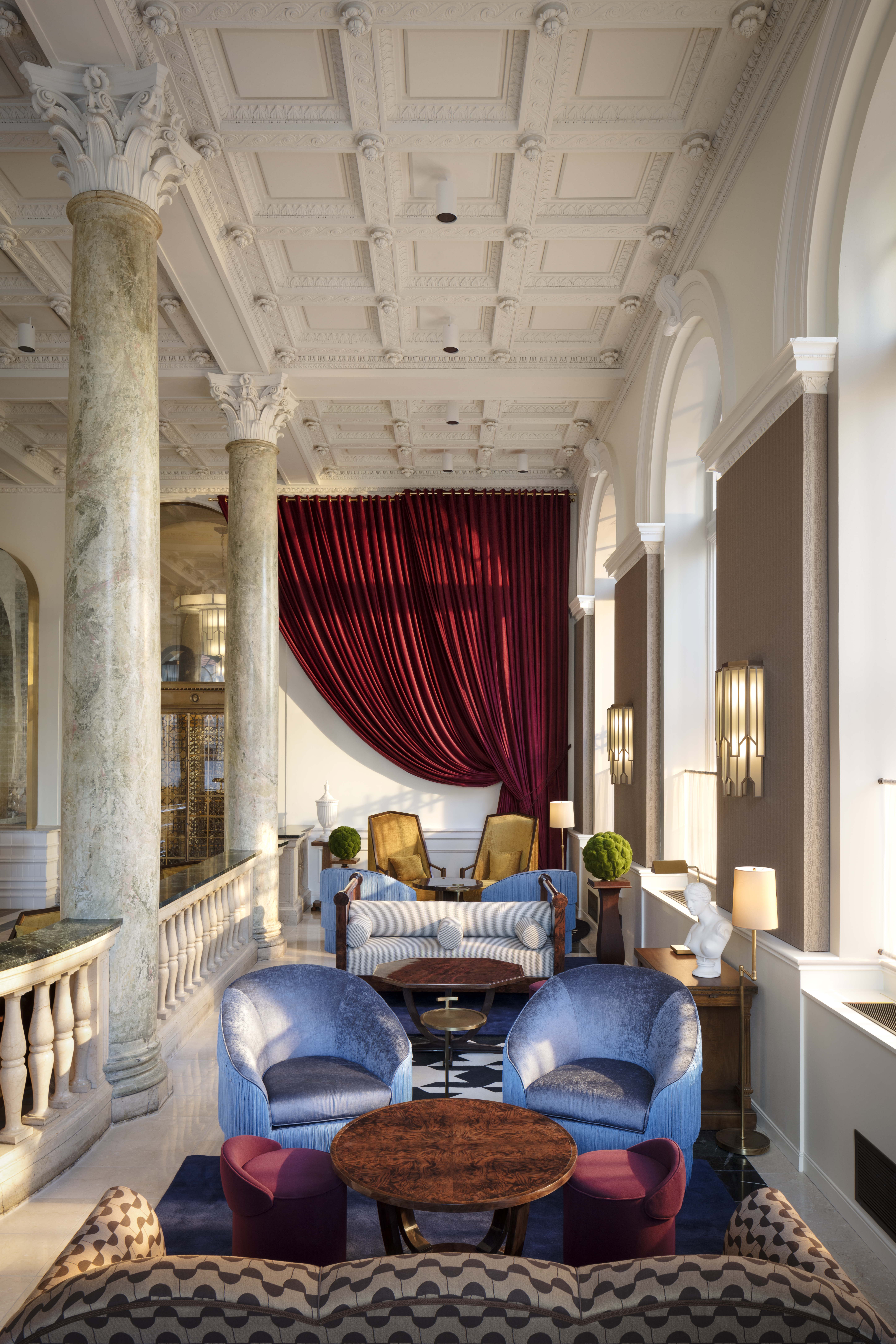 A luxurious lobby with marble columns, a red curtain, and elegant furniture.