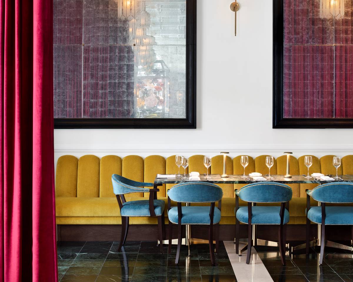 A semi-private dining room with blue chairs and a yellow sofa set for an intimate event with elegant table setting.