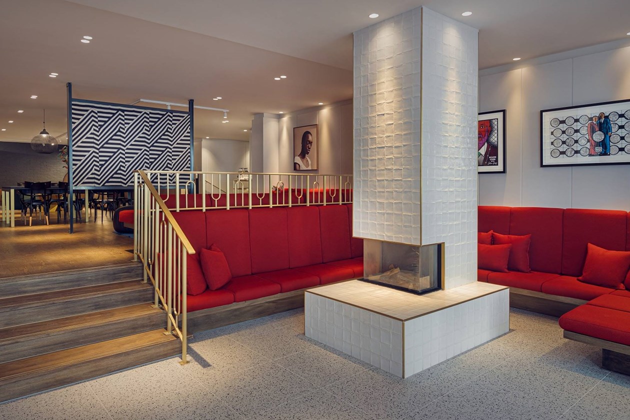 A modern lounge of Kimpton De Witt hotel with red banquette seating, a white fireplace, and geometric artwork on the walls.