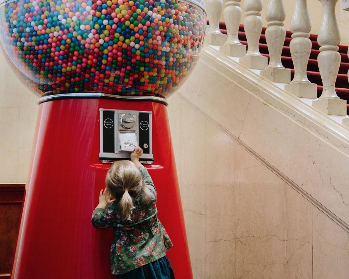 a young girl inserting a coin into a giant gumball machine