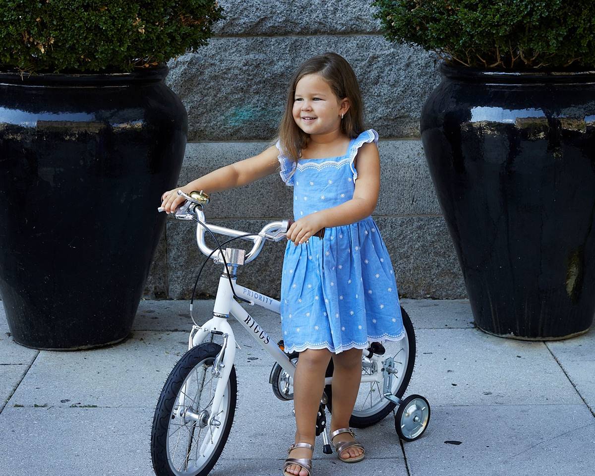 A young girl posing with a bicycle in front of a stone wall and potted plants.