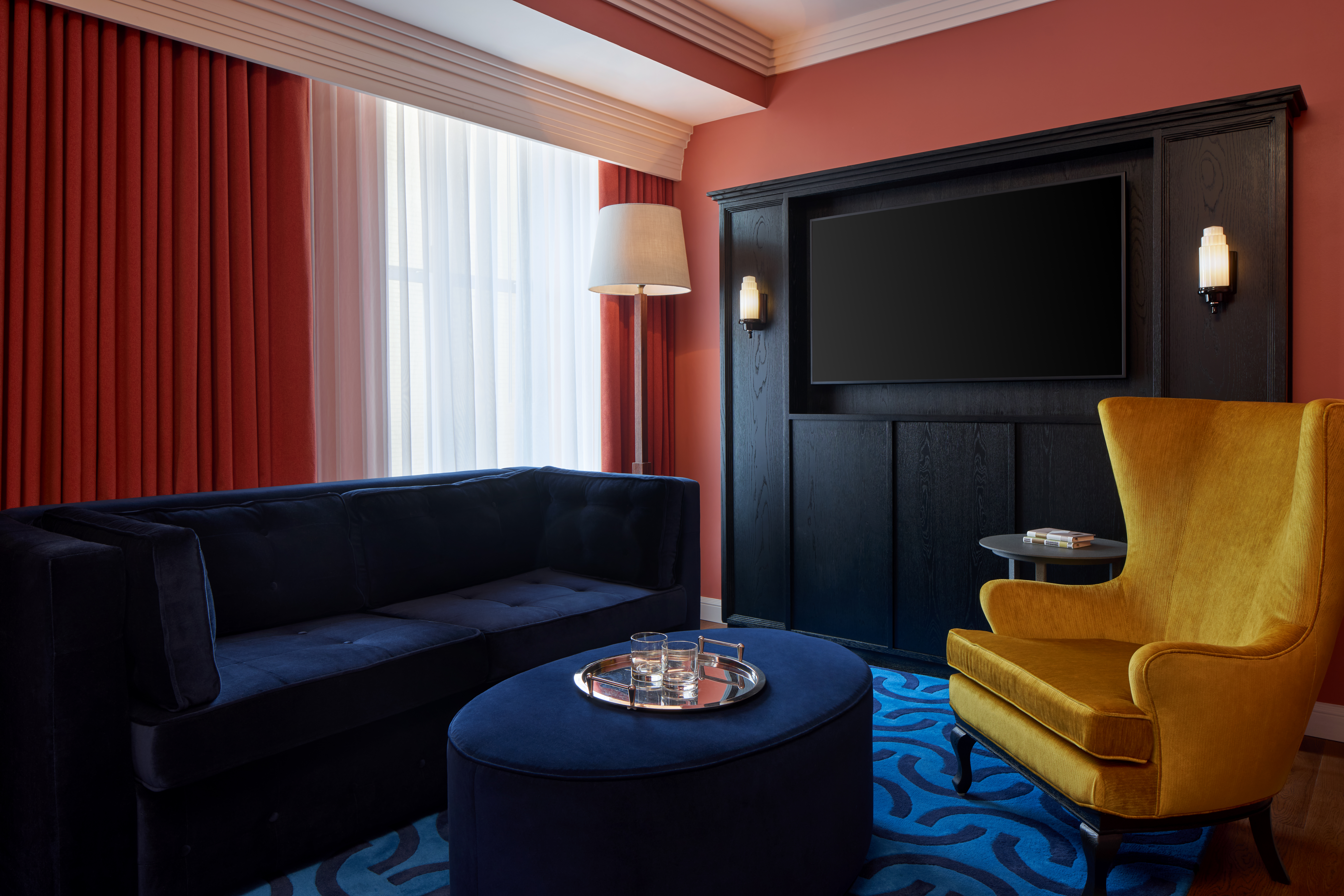 A living room with a blue sofa, yellow chair, and a large TV on the wall.