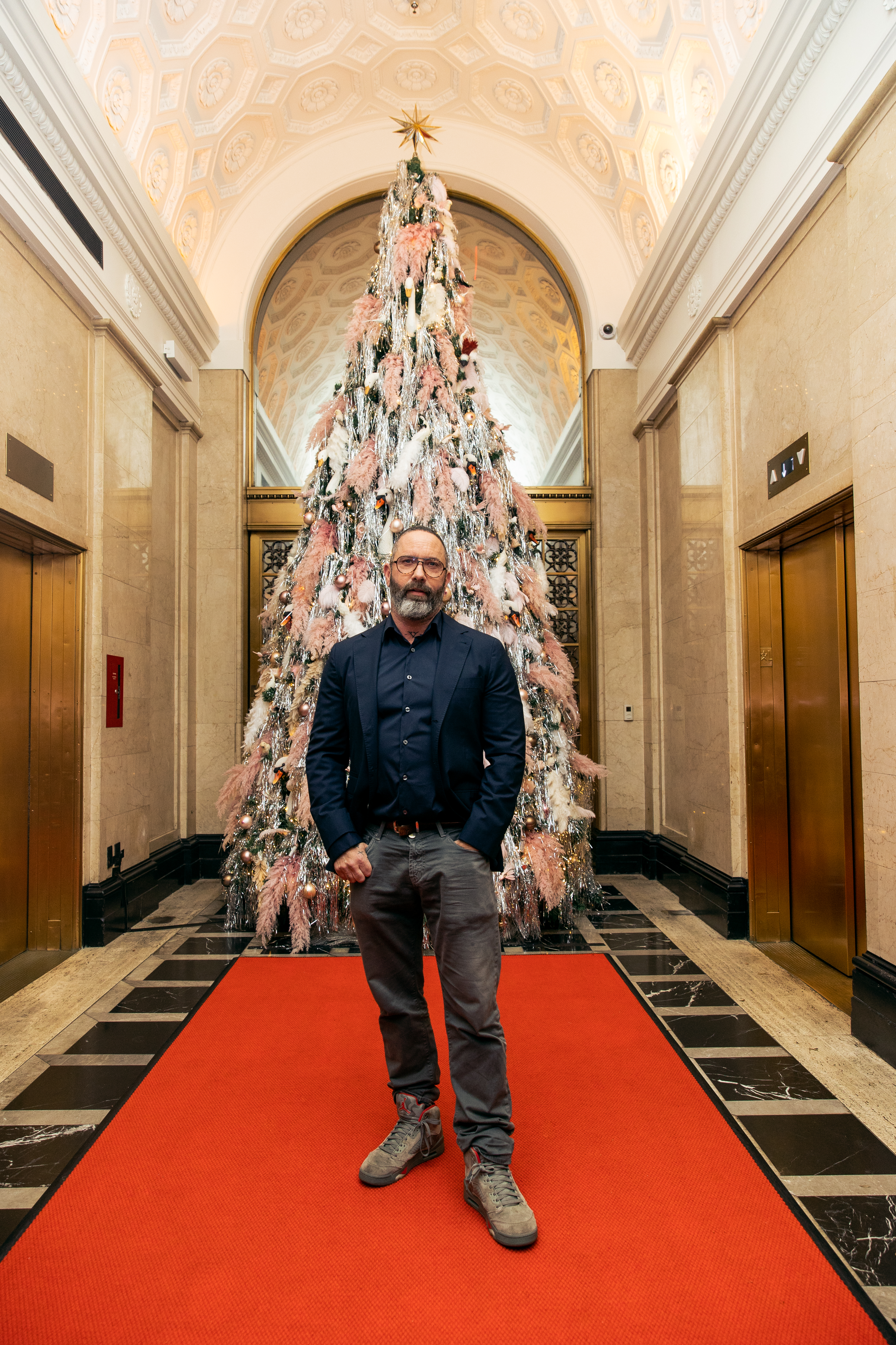 Picture of a man standing in front of a decorated Christmas tree at the Riggs DC hotel, highlighting the festive atmosphere.