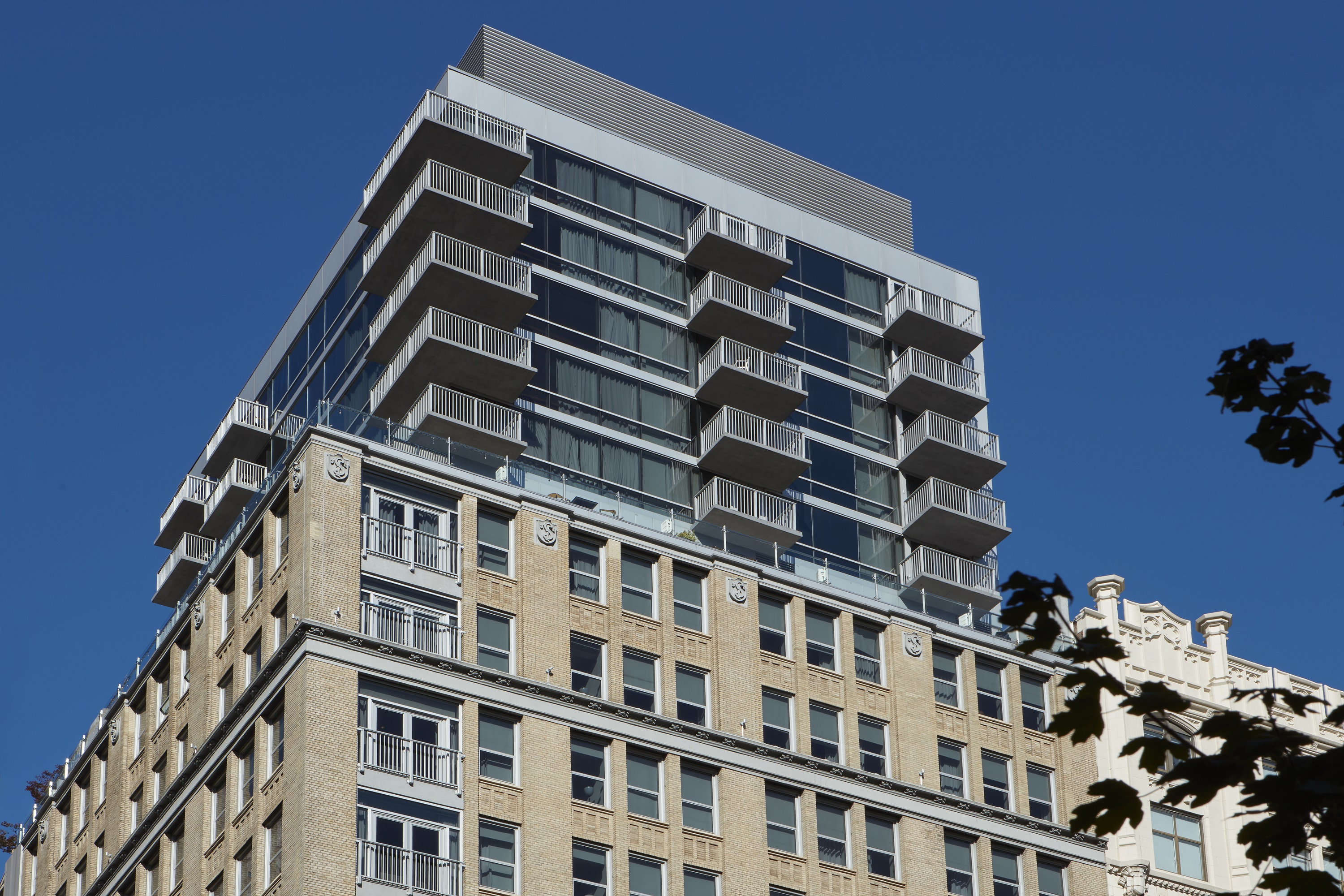 View of the modern building of Hotel Park Ave NYC with balconies stacked over a historic brick façade.