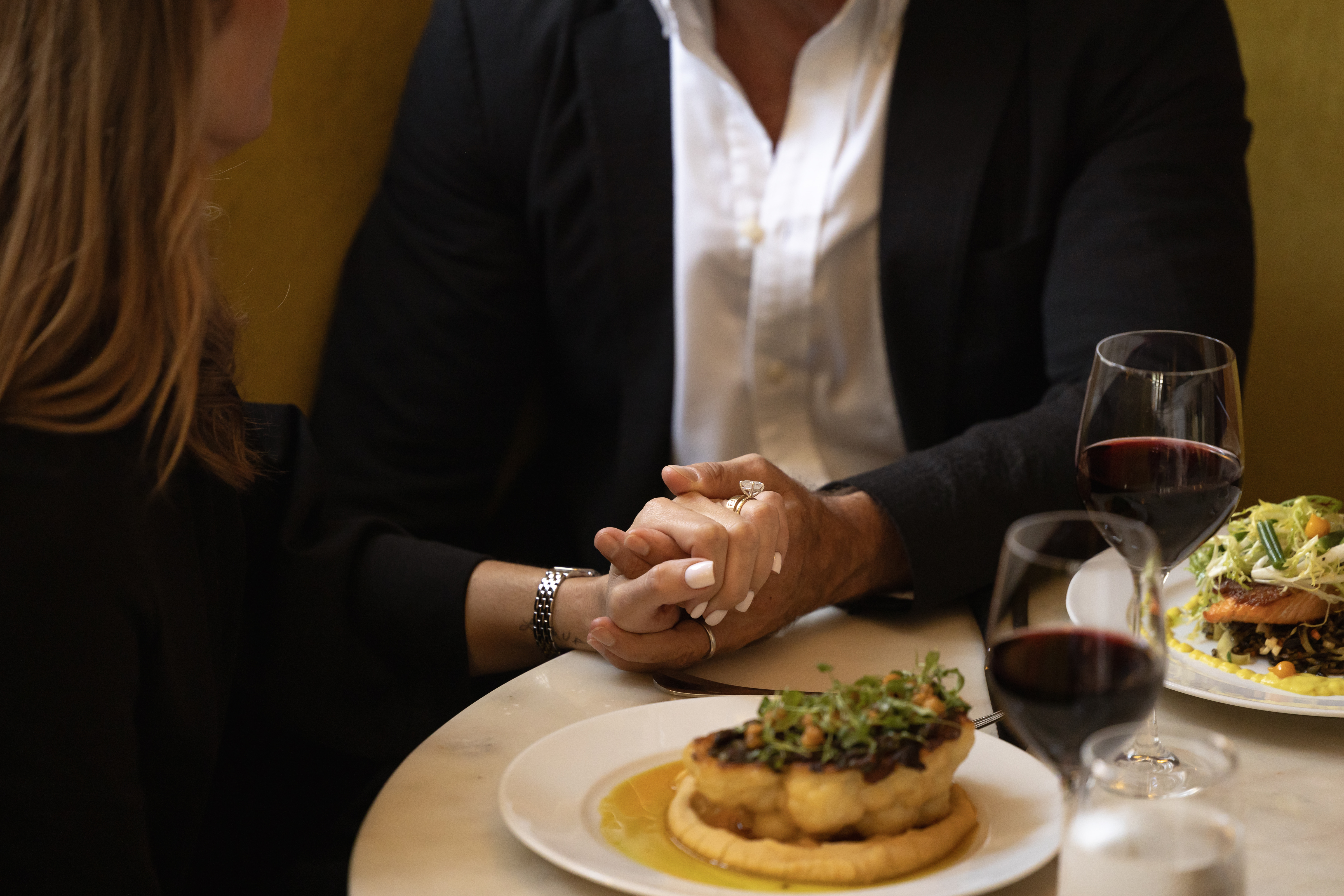 Couple holding hands over a candlelit dinner with wine glasses and gourmet dishes, exuding romance and intimacy.