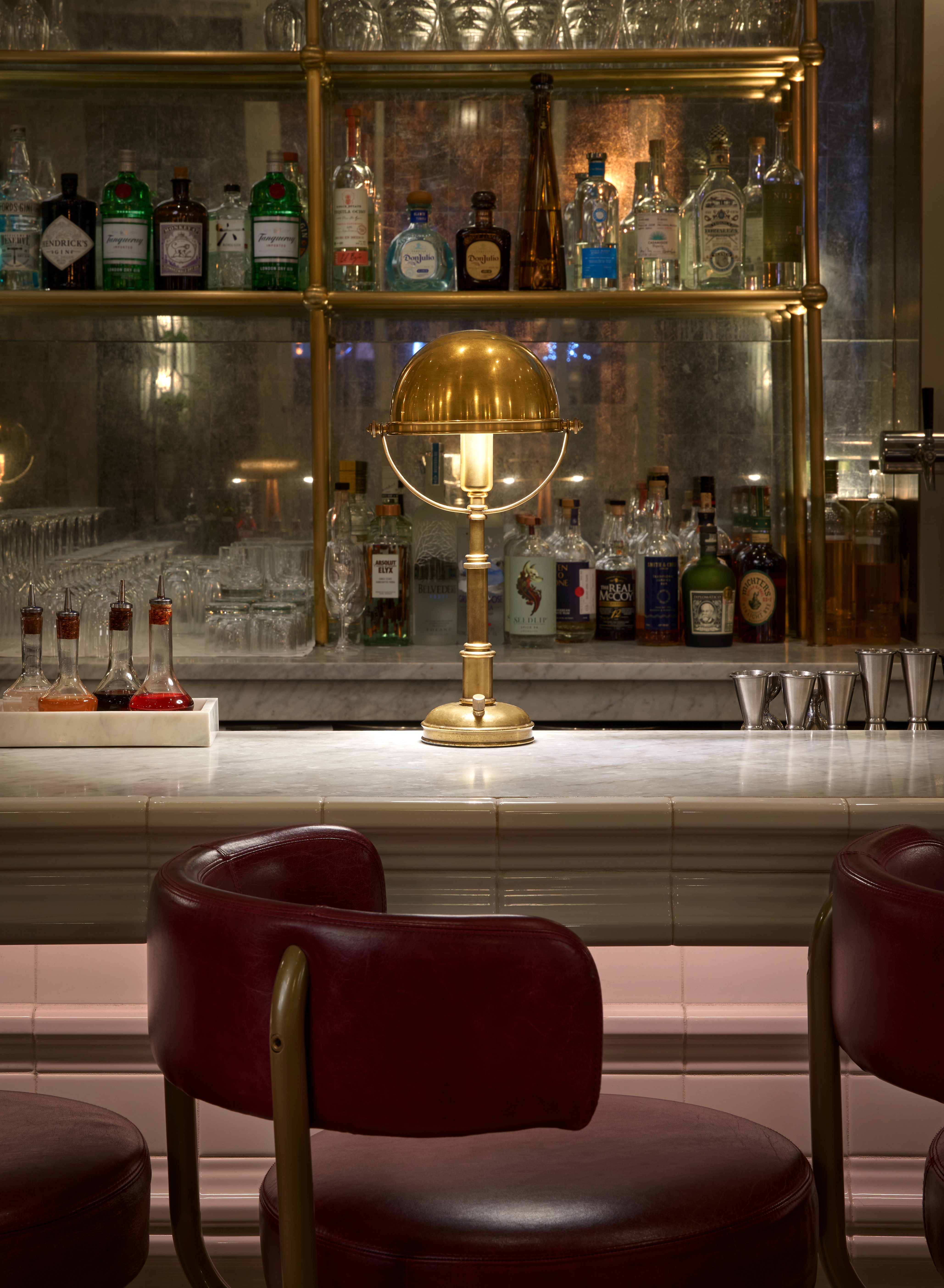 A marble bar top at Café Riggs, with an elegant lamp in the middle and bottles on the shelf in the background.