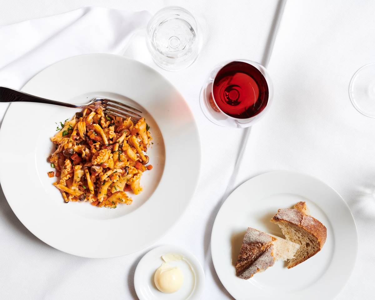 A beautifully plated pasta dish accompanied by a glass of wine and bread showcasing fine dining at Riggs DC.